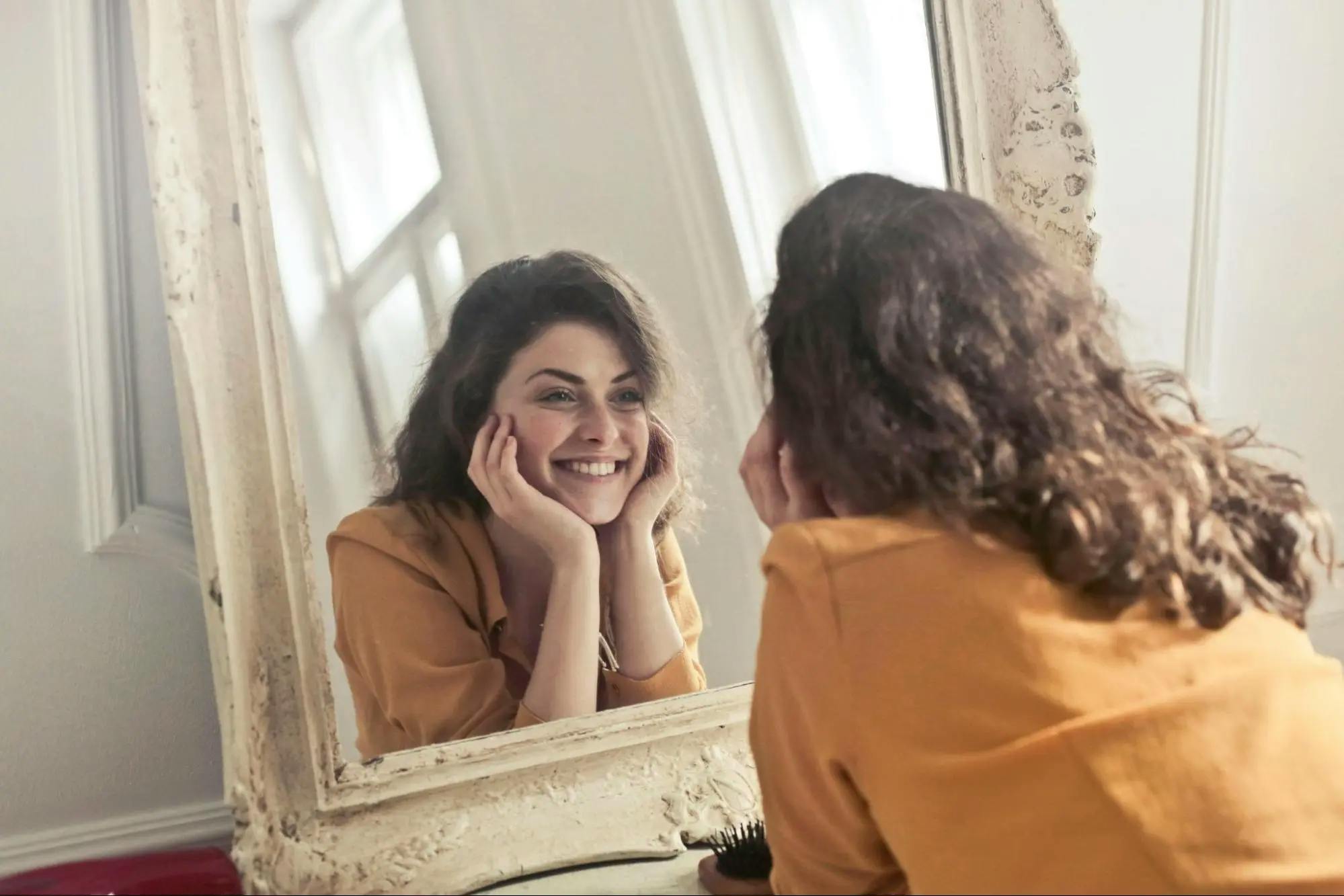 A girl in mustard shirt smiling in the mirror