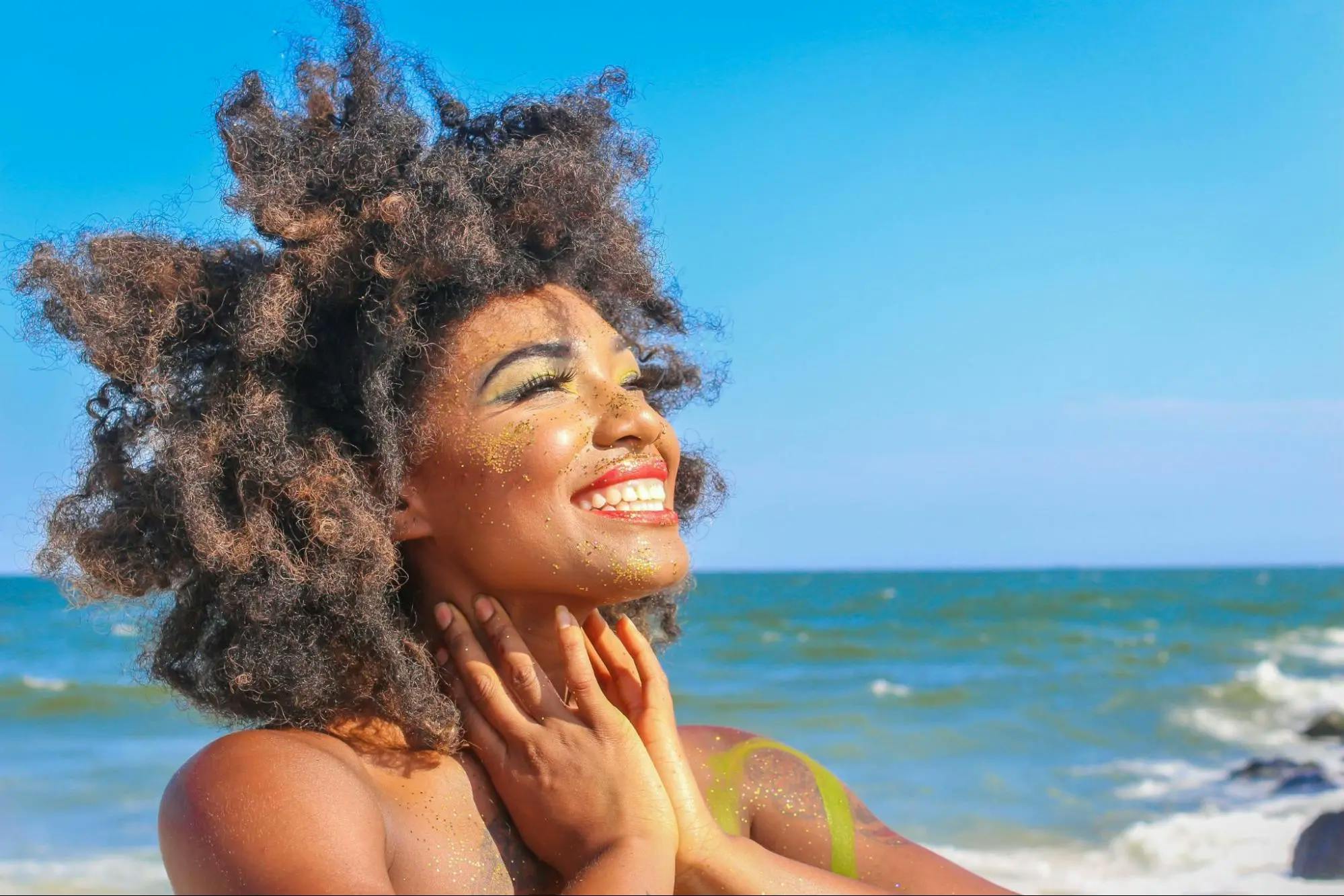 A woman at the beach, smiling as she gazes at the sun